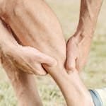 A man outdoors massaging his calf, dealing with muscle pain during sports activities.