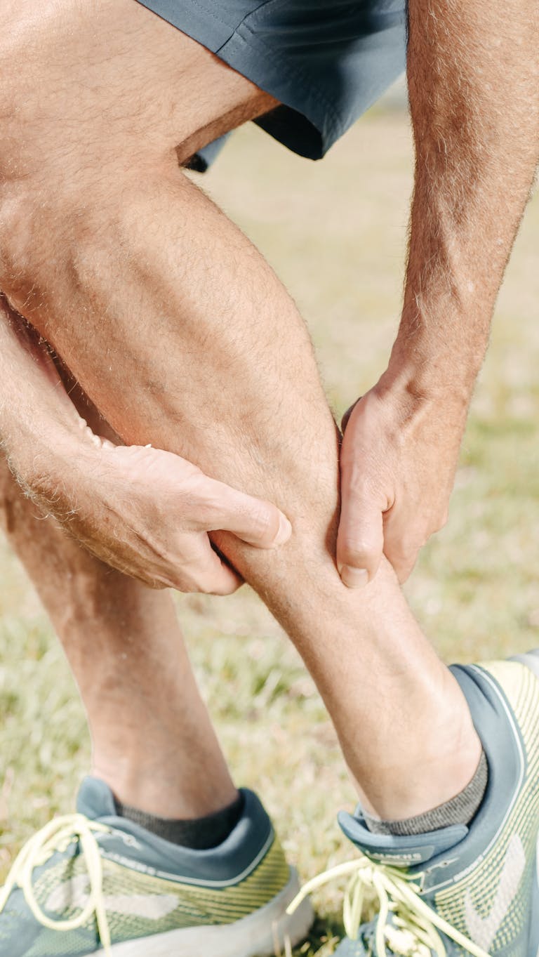 A man outdoors massaging his calf, dealing with muscle pain during sports activities.