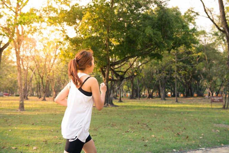 A woman jogging through a forest park in the early morning sunshine, enjoying a healthy lifestyle.