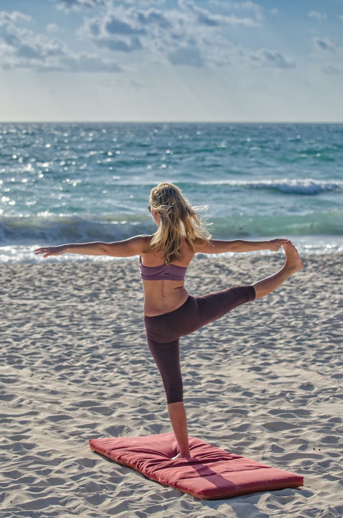 A woman performs yoga on a sandy beach at sunrise, embracing wellness and tranquility.