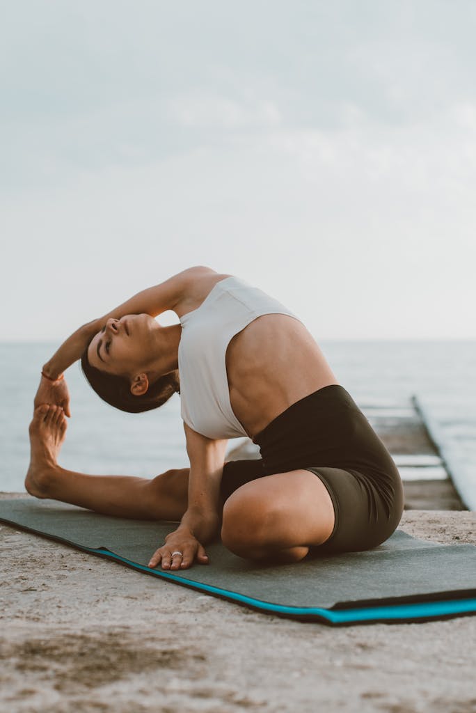 Adult woman practicing yoga on a wooden dock by the sea, promoting wellness and flexibility.