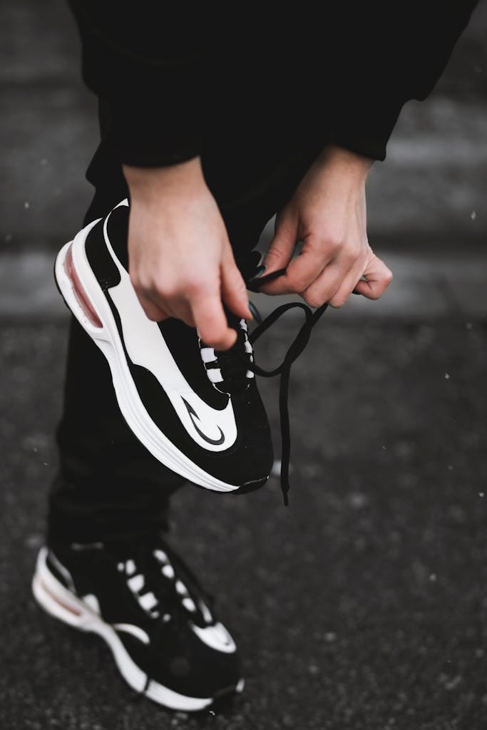 Close-up of an athlete tying black and white sneakers on a street, highlighting fitness and outdoor exercise.