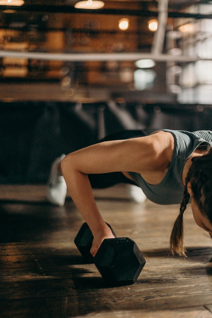 Fit woman doing a dumbbell push-up in a gym, highlighting strength and fitness training.