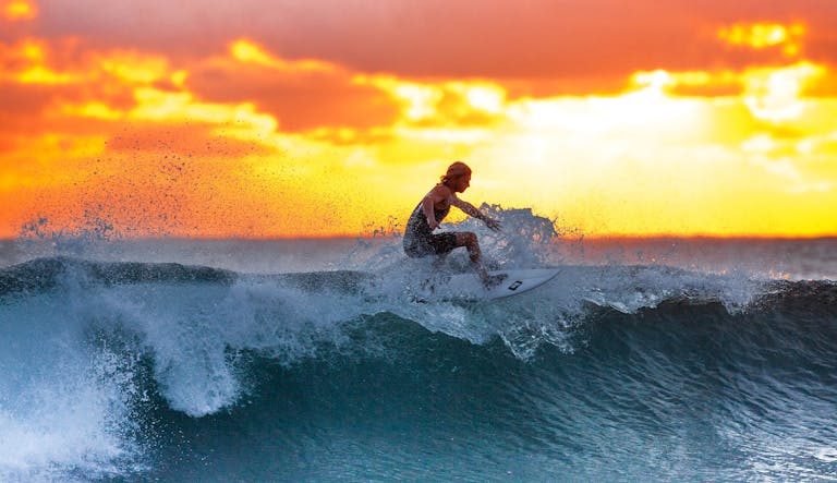 Surfer riding a wave during a stunning sunset, capturing the thrill of water sports.