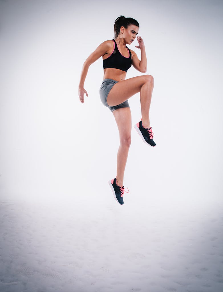 Woman in black sports bra and gray shorts performing a jump during workout.