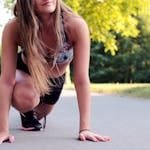 Young woman in athletic wear ready to sprint on a sunny day.