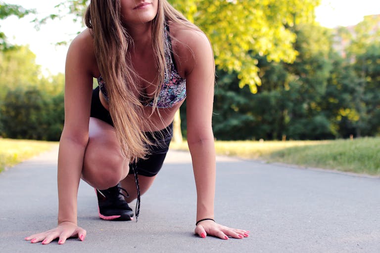 Young woman in athletic wear ready to sprint on a sunny day.